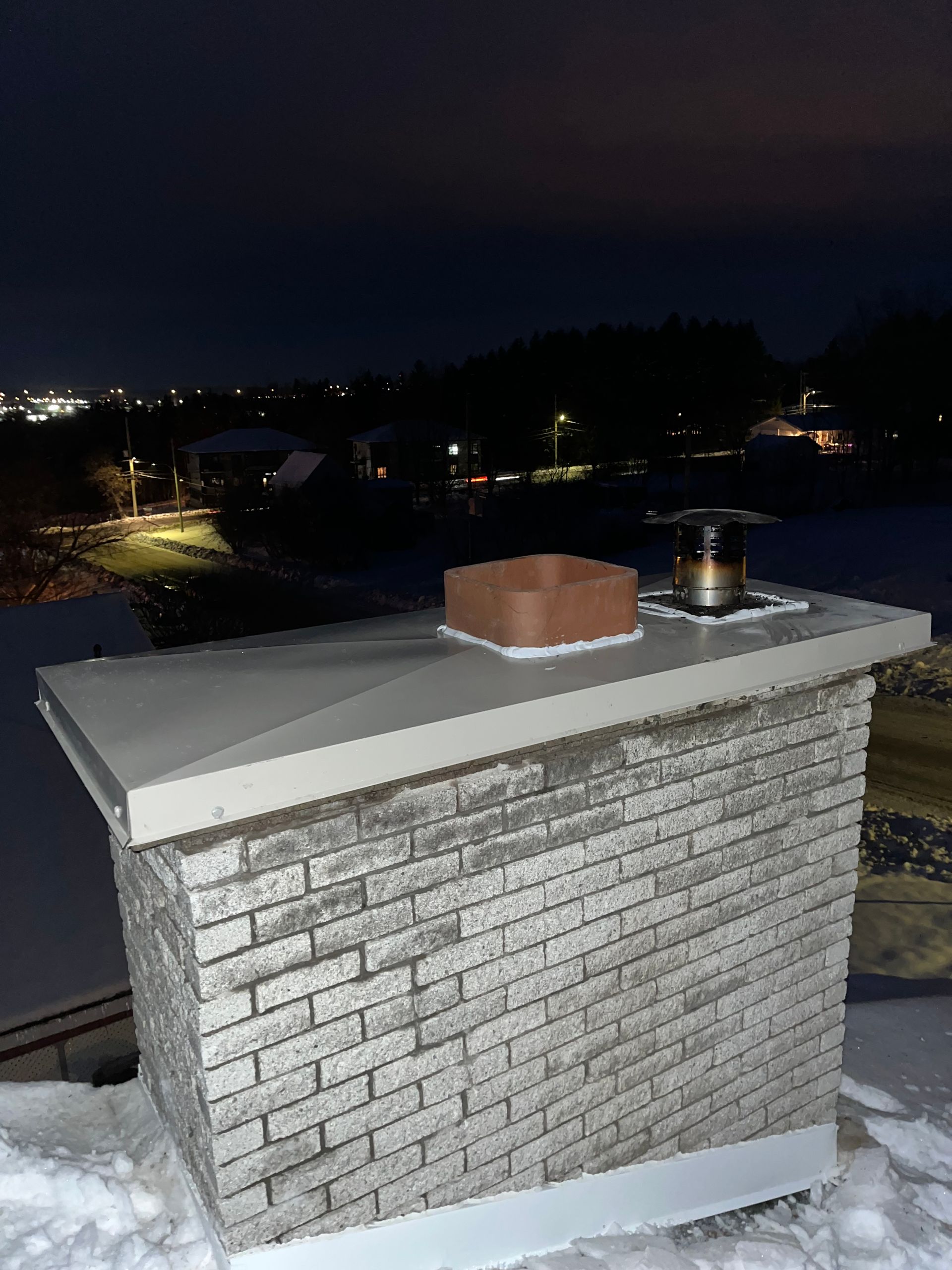 Une cheminée en brique se trouve au sommet d'un toit couvert de neige la nuit.