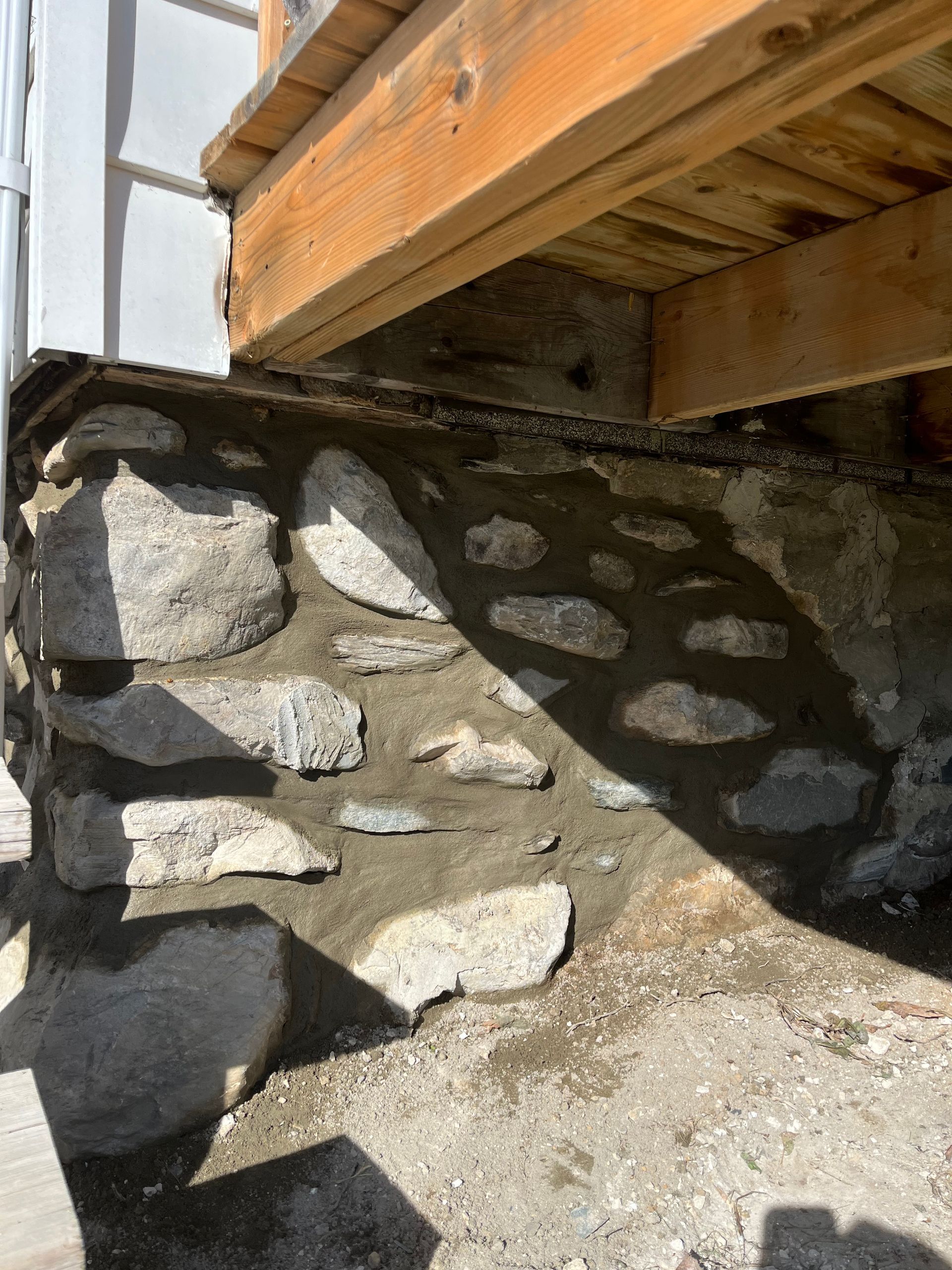 Un mur en pierre est en cours de construction sous une terrasse en bois.
