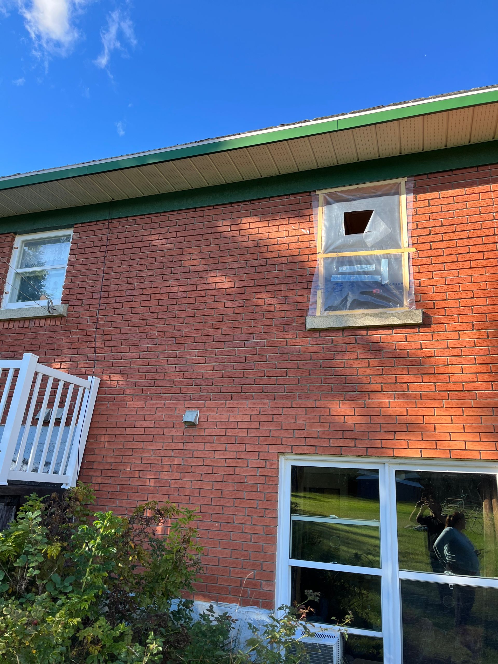 Une maison en brique avec une fenêtre cassée et un toit vert.