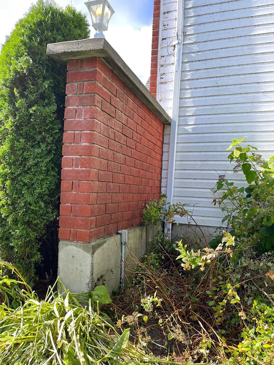 Un mur de briques rouges jouxte une maison blanche.