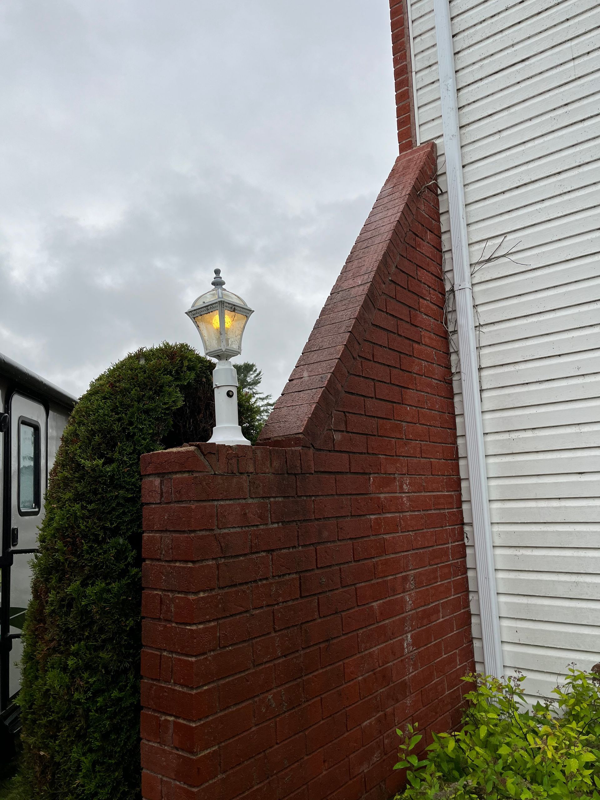 Un lampadaire sur un mur de briques à côté d’une maison blanche.