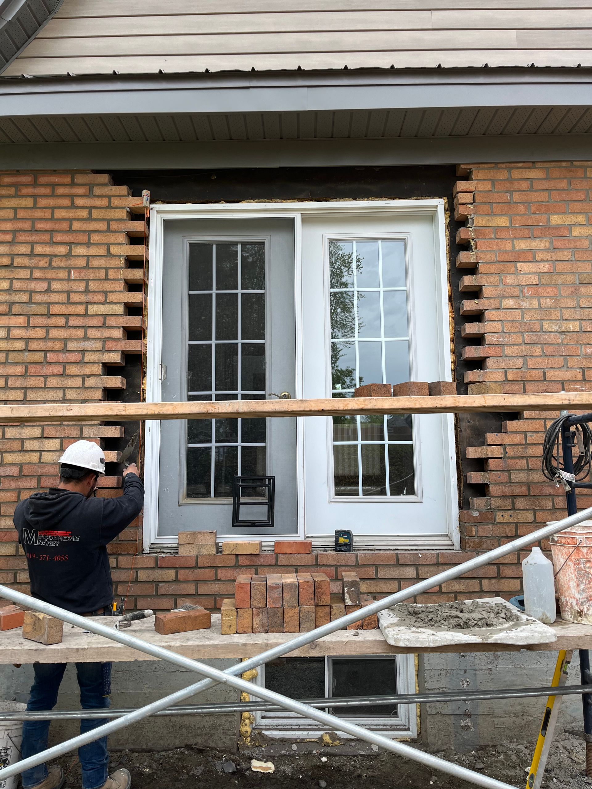 Un homme travaille sur un mur de briques à côté d’une fenêtre.