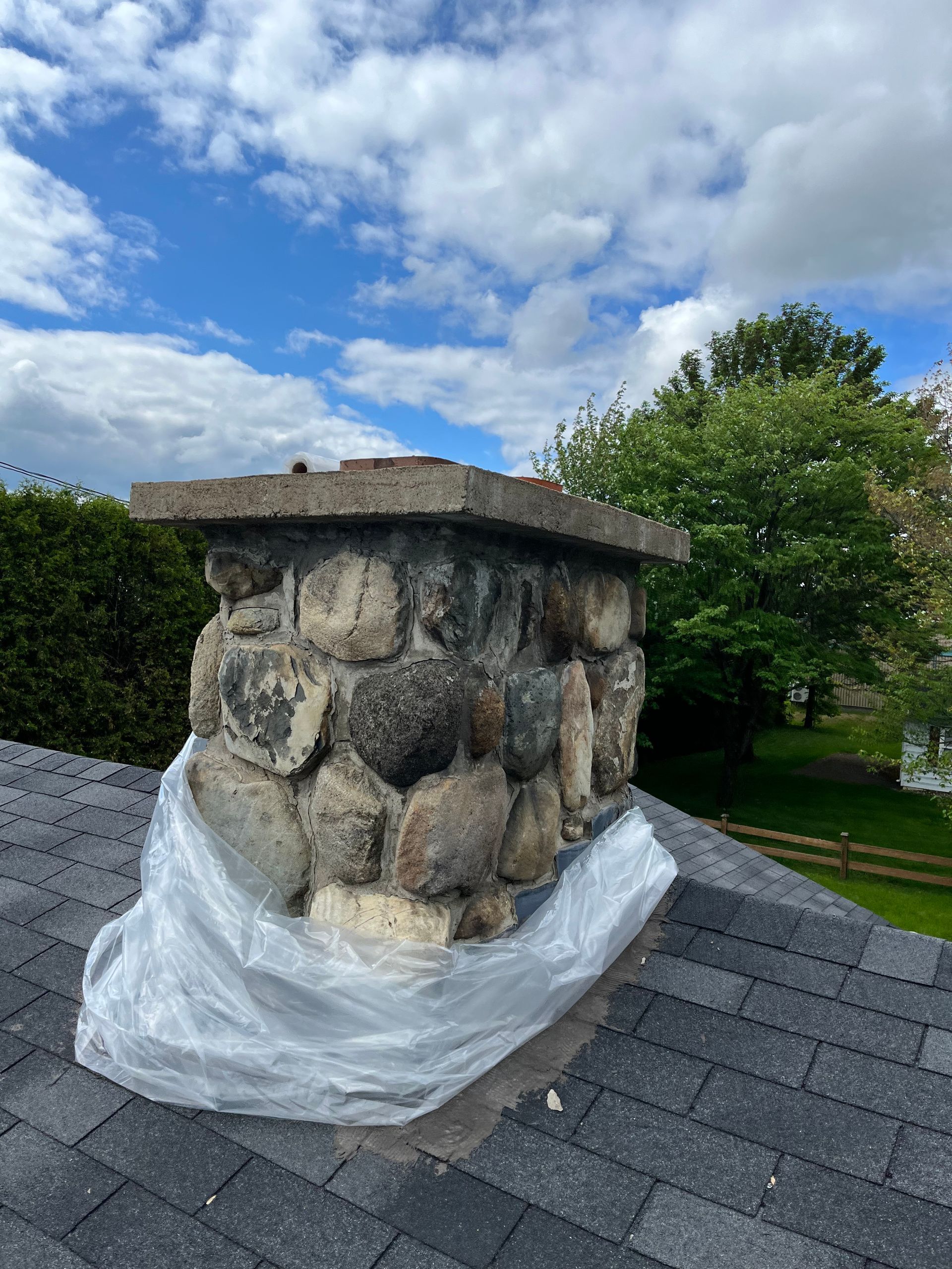 Une cheminée en pierre est enveloppée dans du plastique et posée sur un toit.