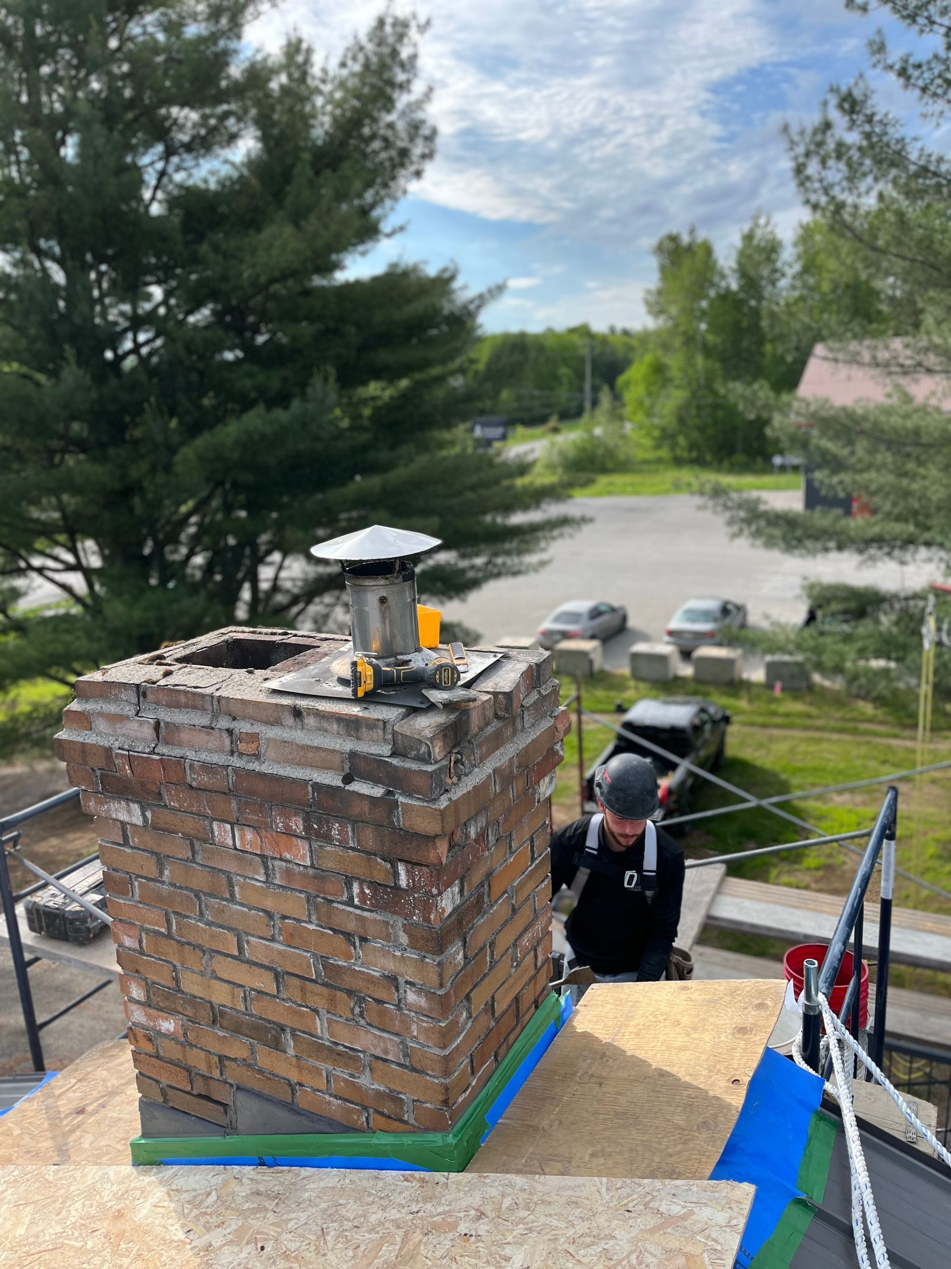 Un homme travaille sur une cheminée en brique au sommet d'un toit.