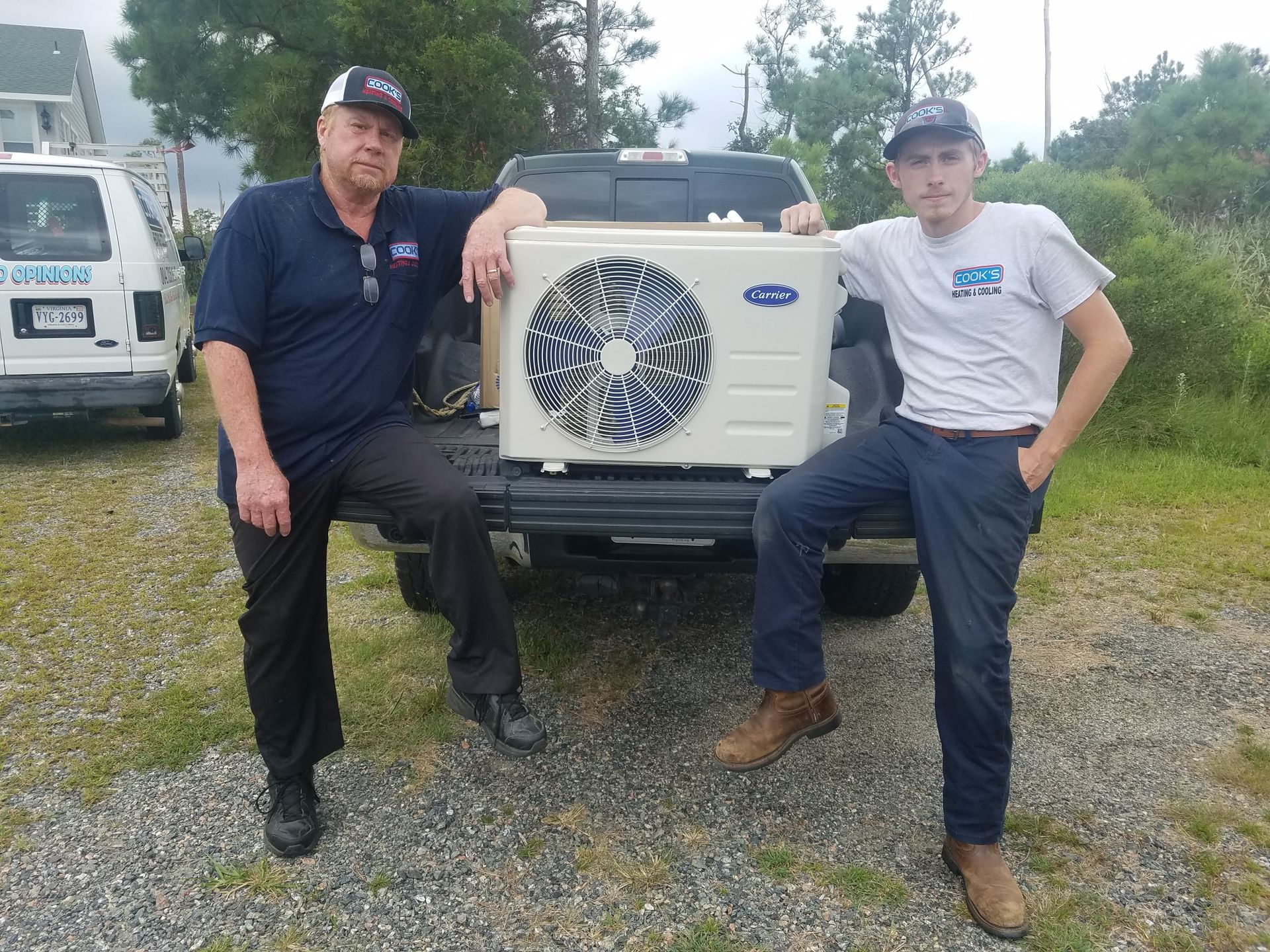 Two men are standing next to a truck holding an air conditioner.