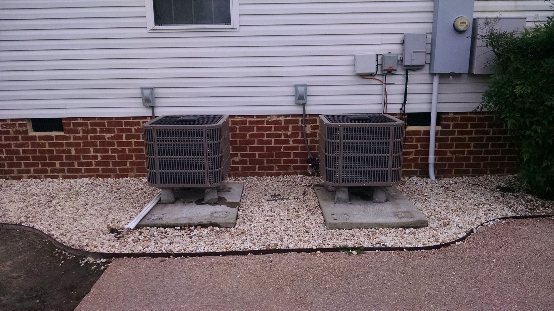 Two air conditioners are sitting outside of a brick house.