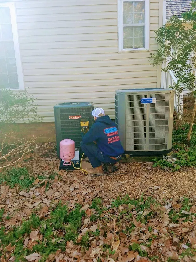 A man is working on an air conditioner outside of a house.
