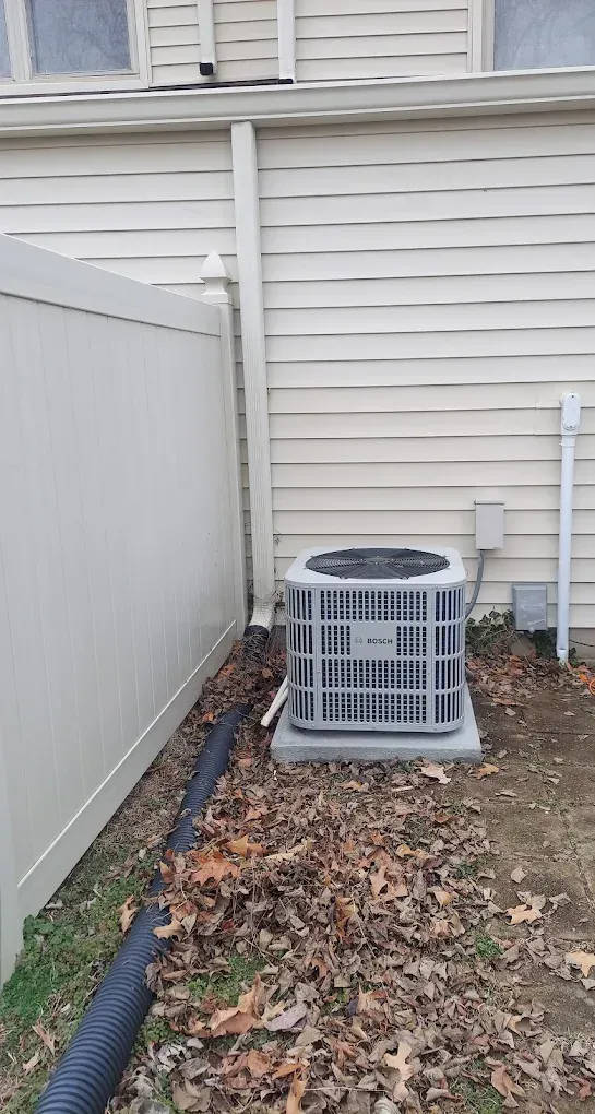 An air conditioner is sitting on the side of a house next to a fence.