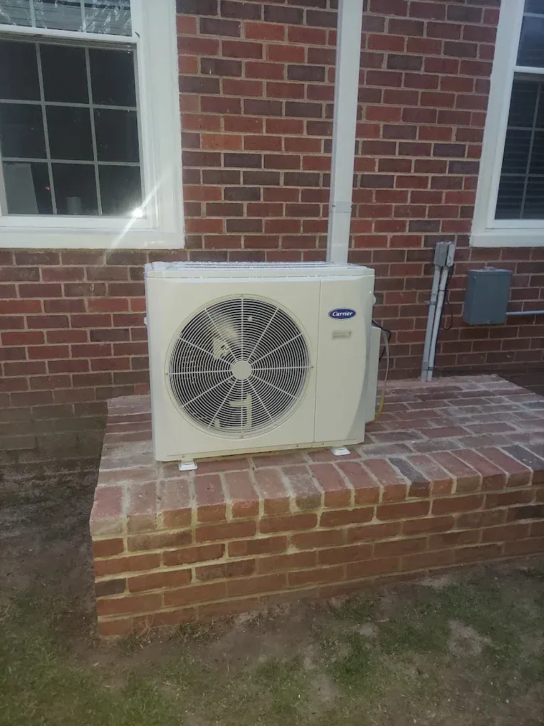 A white air conditioner is sitting on top of a brick wall.