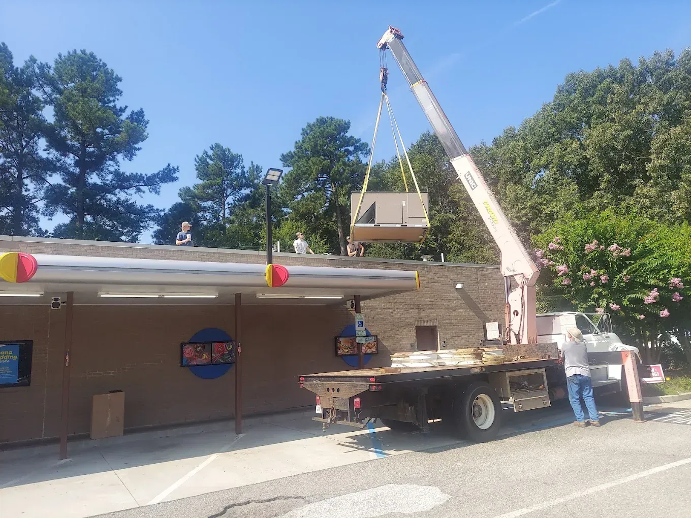 A crane is lifting a piece of wood from the roof of a building.
