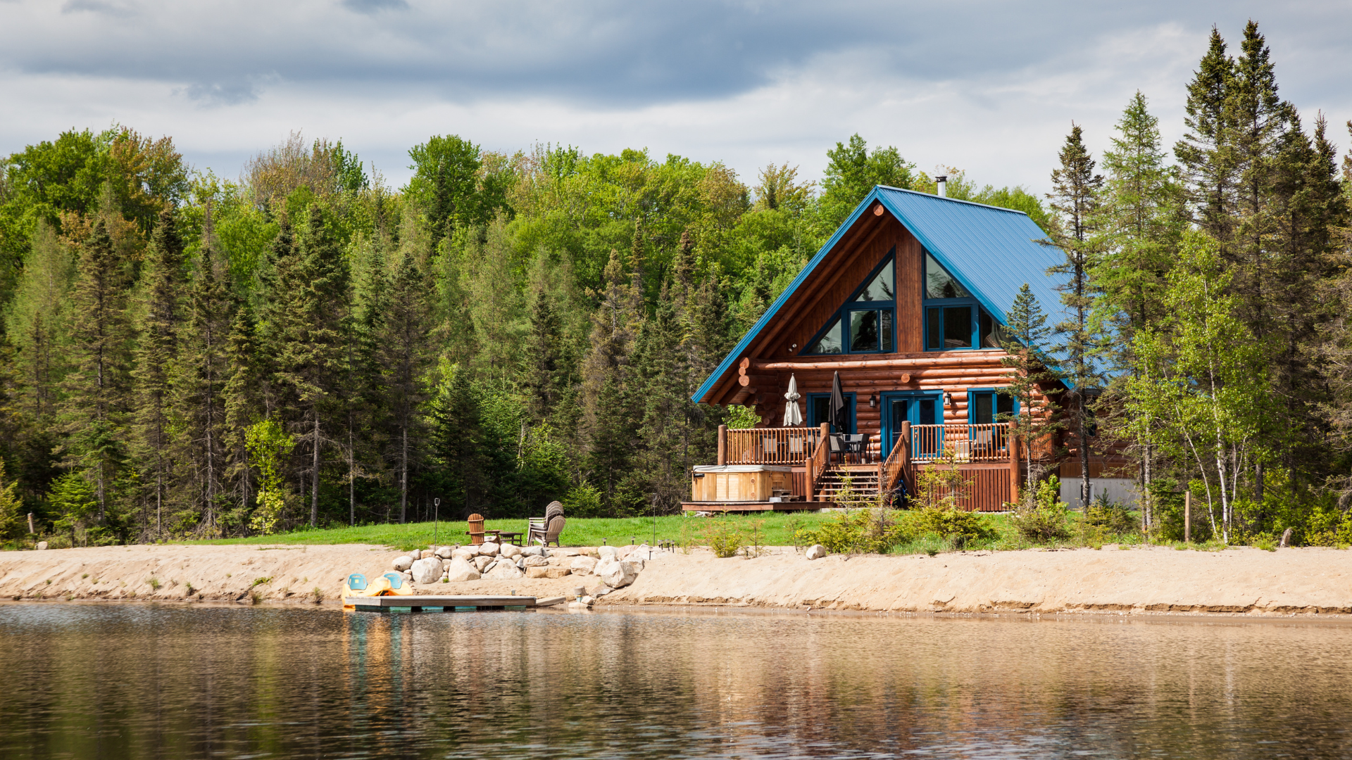 a log cabin with a blue roof is sitting on the shore of a lake surrounded by trees .