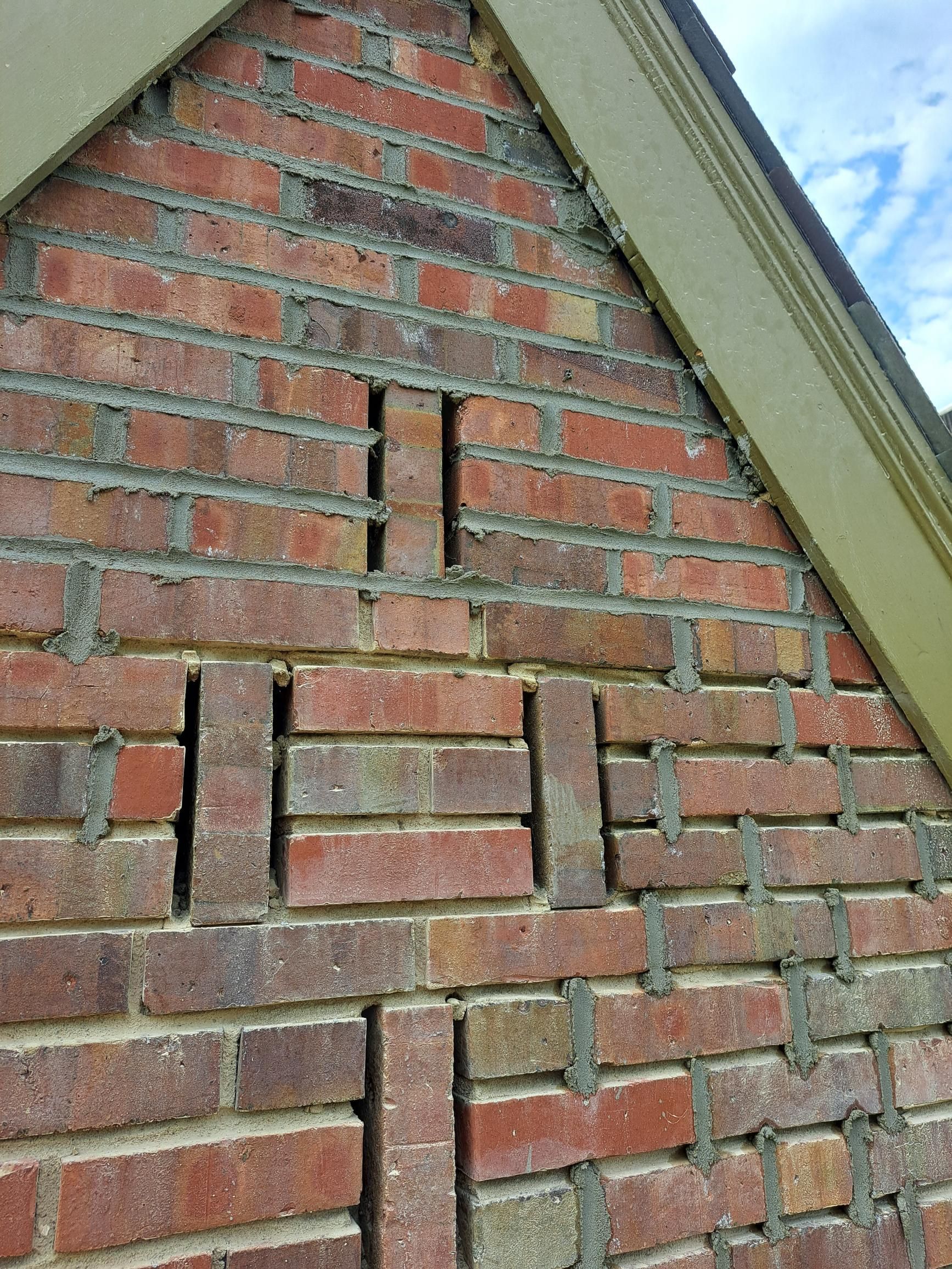 Brick wall with geometric air vents; red bricks and gray mortar, set against a green-trimmed roof and sky.