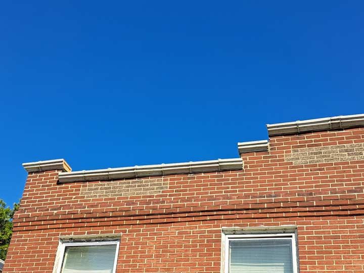 Brick building exterior with a bright blue sky background. Red bricks with white window frames.