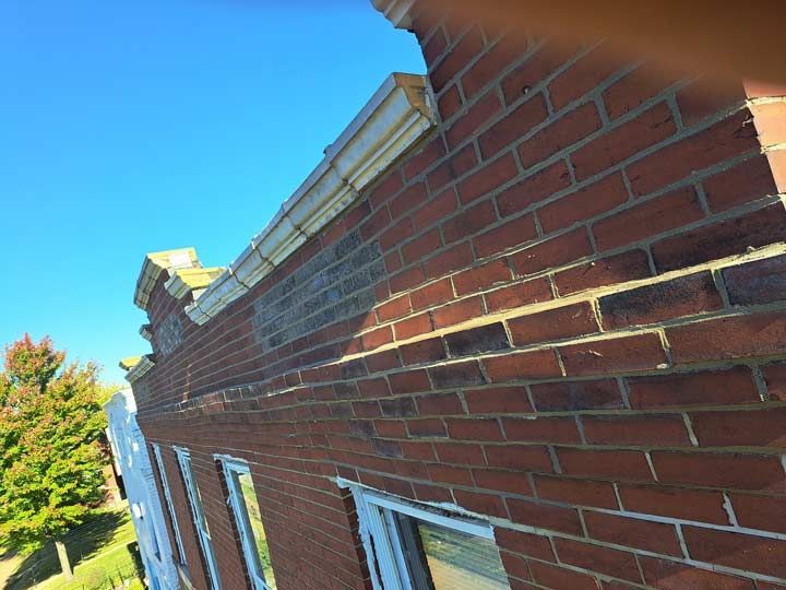 Brick building exterior with reddish-brown bricks, white trim, and a clear blue sky. Sunlight casts shadows.