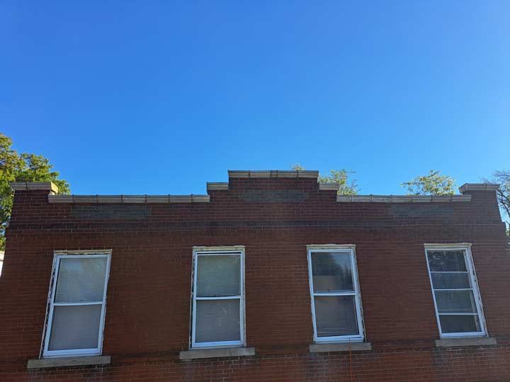 Brick building with four windows under a clear, blue sky. The building has a decorative brick parapet.