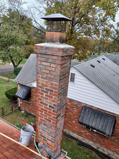 Brick chimney on a red-roofed house, with a metal cap. A bucket and hose sit nearby.