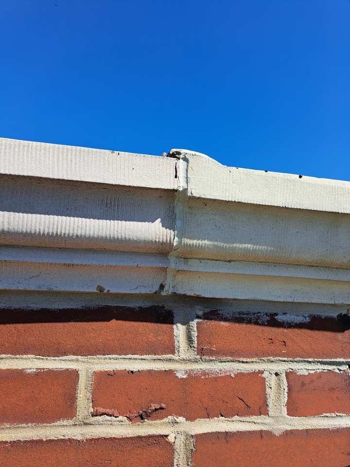 Close-up of a red brick wall with a white, decorative concrete ledge against a clear blue sky.