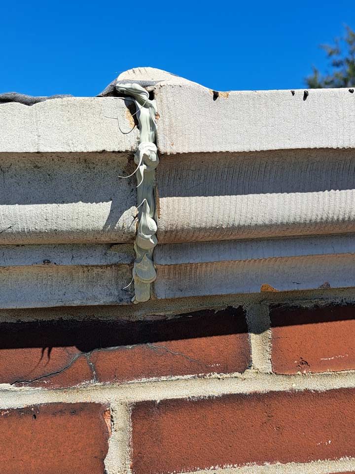 Close-up of a brick wall with a concrete ledge on top. Light-colored sealant oozes from a crack between the concrete blocks.