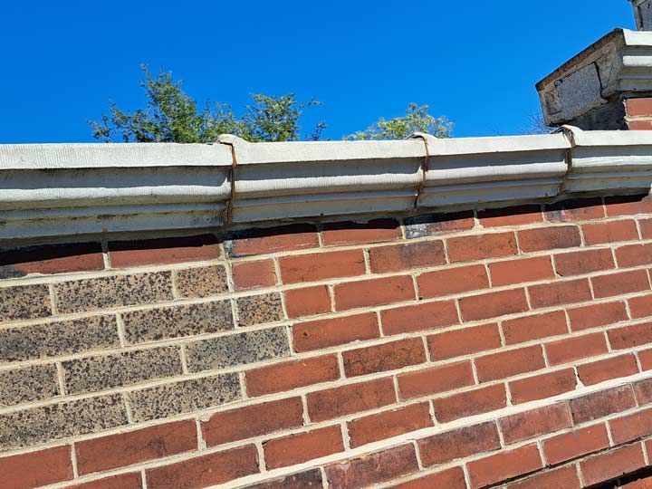 Red brick wall with a gray decorative top, against a clear blue sky. Some darker bricks are visible on the left side.