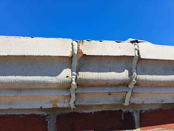White painted guttering attached to a brick wall, with a clear blue sky above. The guttering is held in place by white brackets.