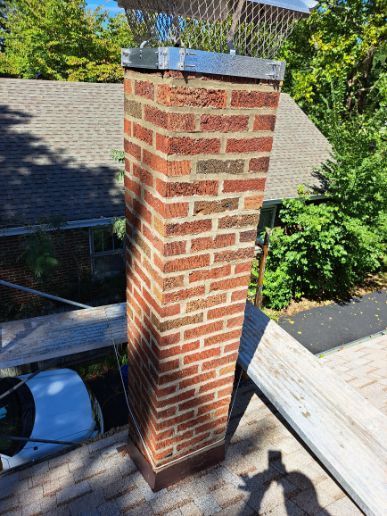 Brick chimney with a metal cap on a roof. The chimney is slightly leaning.