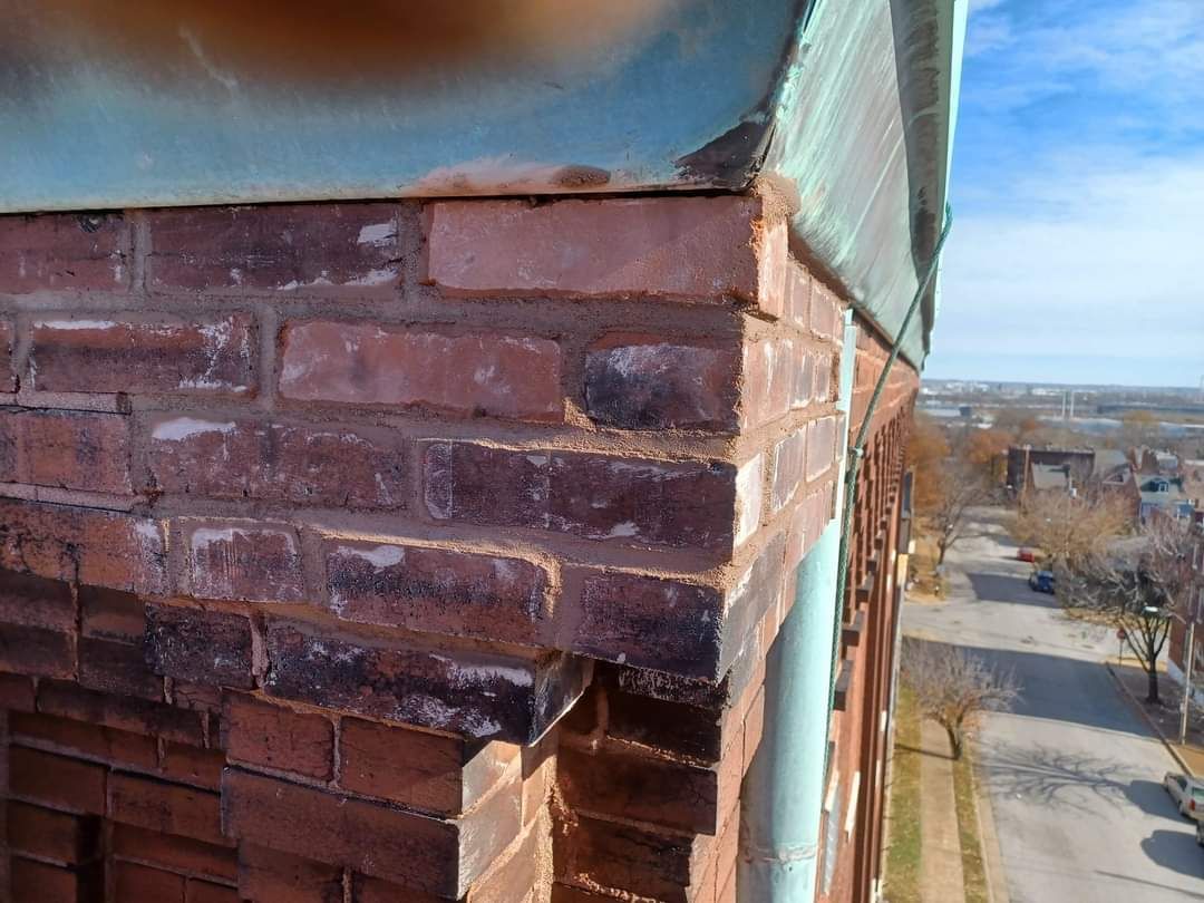 Close-up of a brick building corner with a copper roof. Red brick and faded copper contrast against a blue sky.