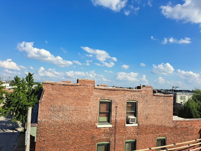 Red brick building with green-framed windows against a blue sky with white clouds. Daytime shot, possible urban setting.