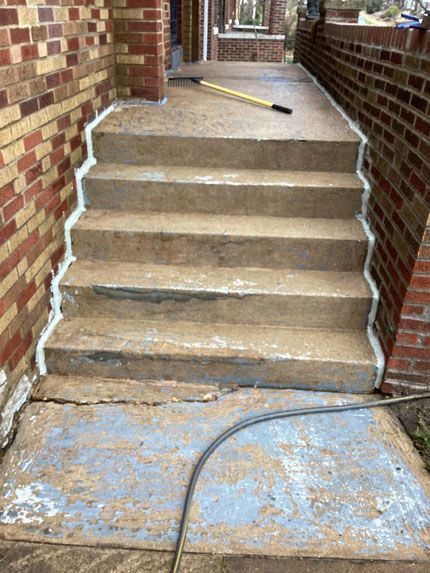Concrete steps with white caulk lines on the sides, leading up to a porch, set between brick walls.