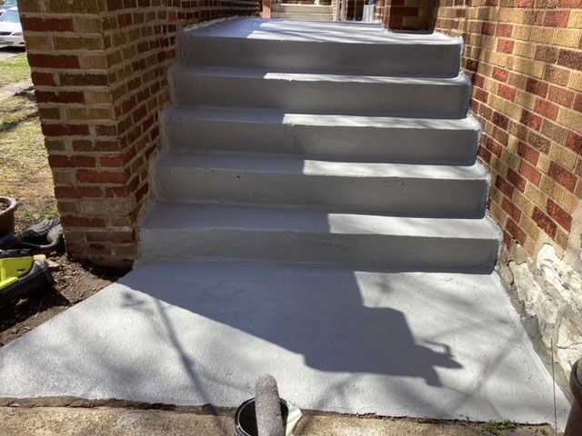 Newly constructed concrete steps leading up to a home's entrance. Gray concrete, bordered by red brick.