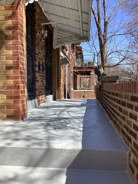 Exterior view of a brick building with gray-painted concrete steps and a narrow walkway beside a low brick wall under a clear sky.
