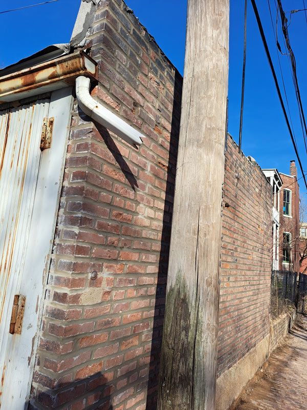Brick building exterior with a rusted metal door and a utility pole on a sunny day.