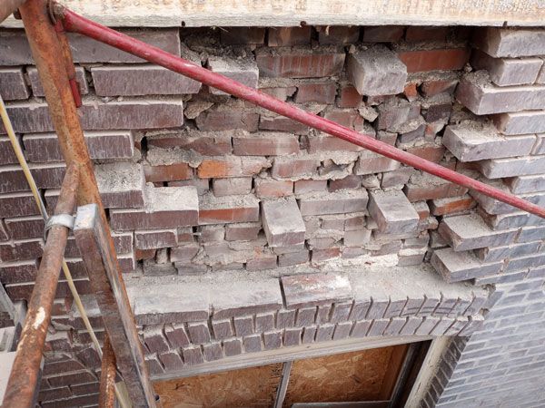 Damaged brick wall section with a red metal support bar, showing crumbling bricks and mortar.