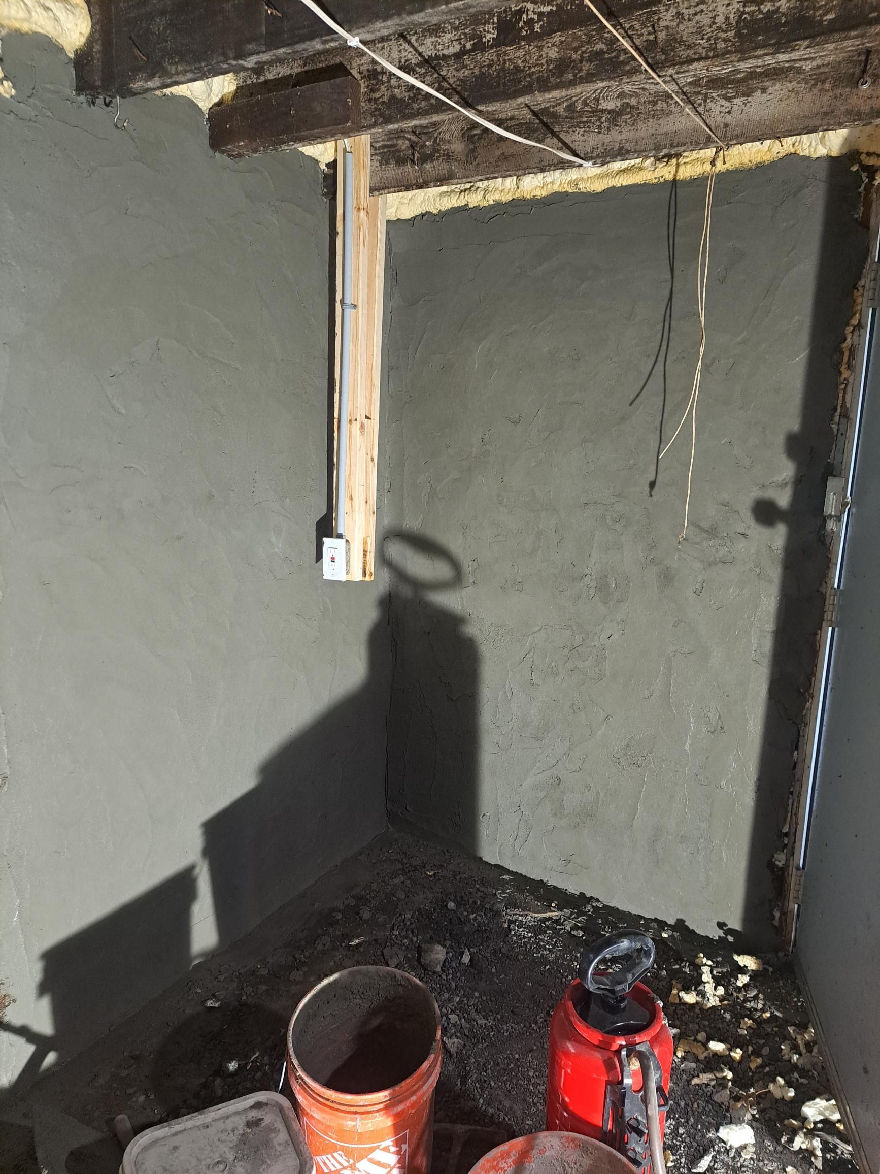 Gray concrete walls and floor in a small enclosure with a wooden support beam and some debris.