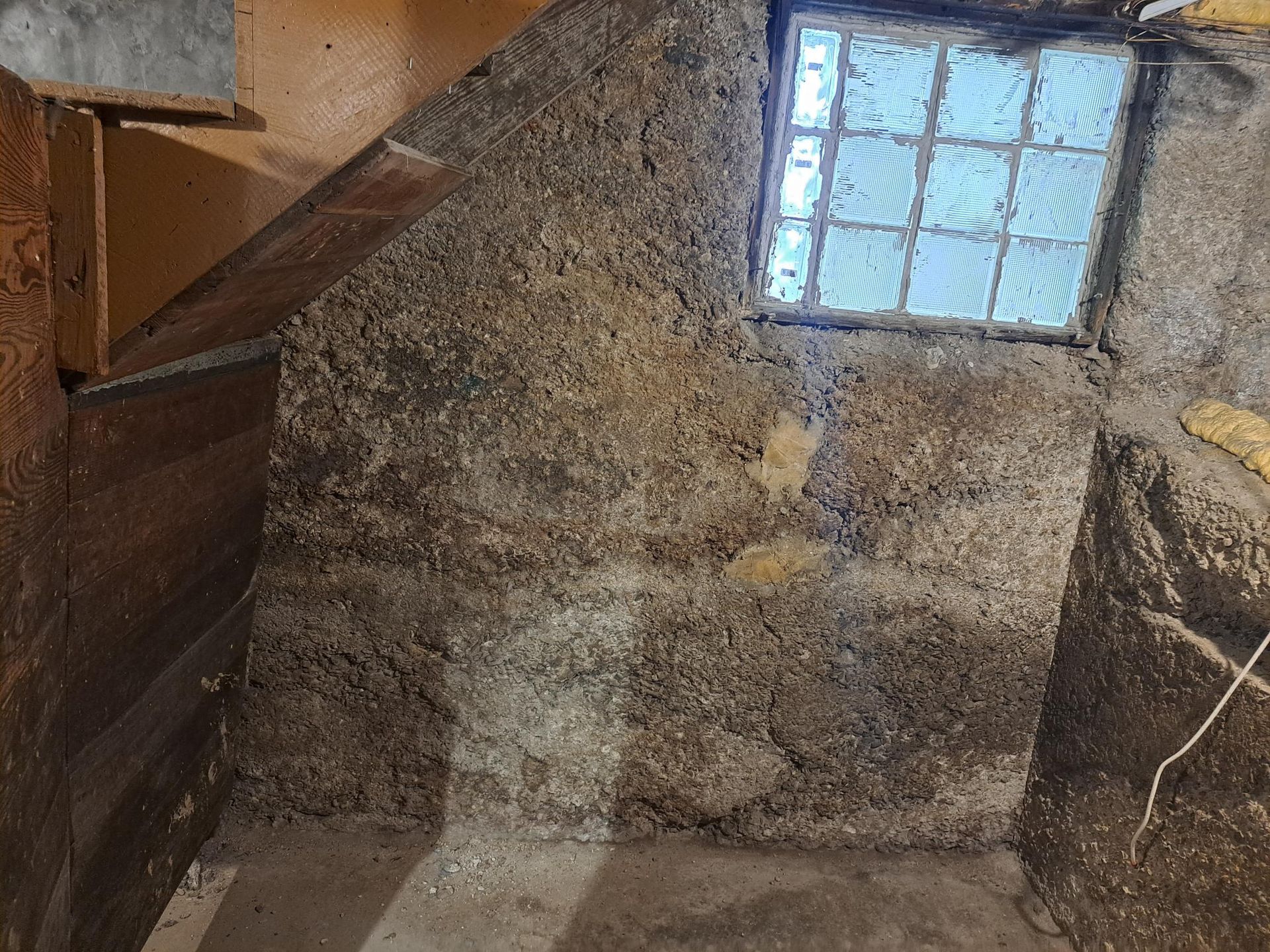 Basement corner with rough, textured concrete walls, a small glass block window, and dim lighting.