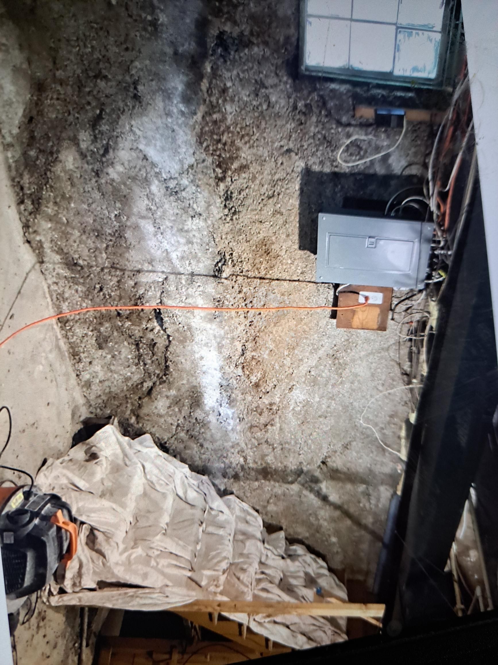 Overhead view of a crawl space.  Concrete floor with wires and electrical boxes.  A tarp covers some materials.