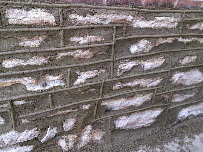 Close-up of a stone wall with grey mortar between the irregularly shaped white stones.  A brick border is at the top.
