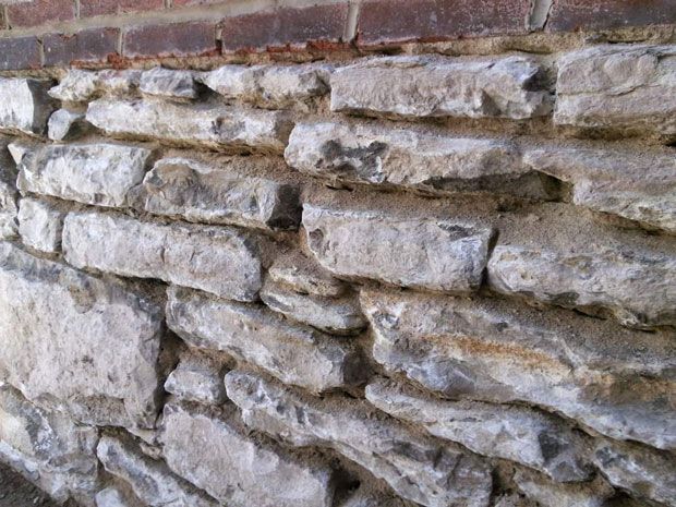 Stone wall with rough, uneven texture, below a row of red bricks.