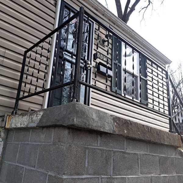 Front view of a house with a concrete block porch and a black metal security door and railing. Beige siding and black shutters.