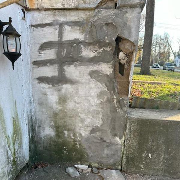 Damaged concrete pillar with patched areas, a missing chunk, and moss. A lamp is mounted on the left side.