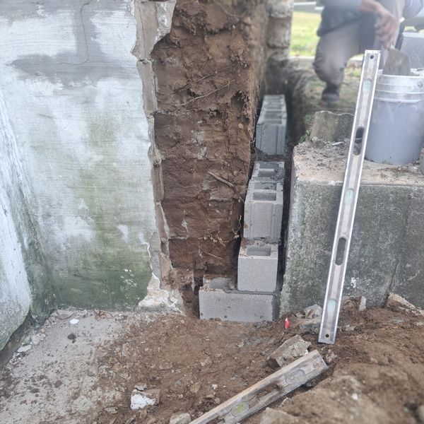 Construction of a concrete block wall next to a damaged wall. A level is used.