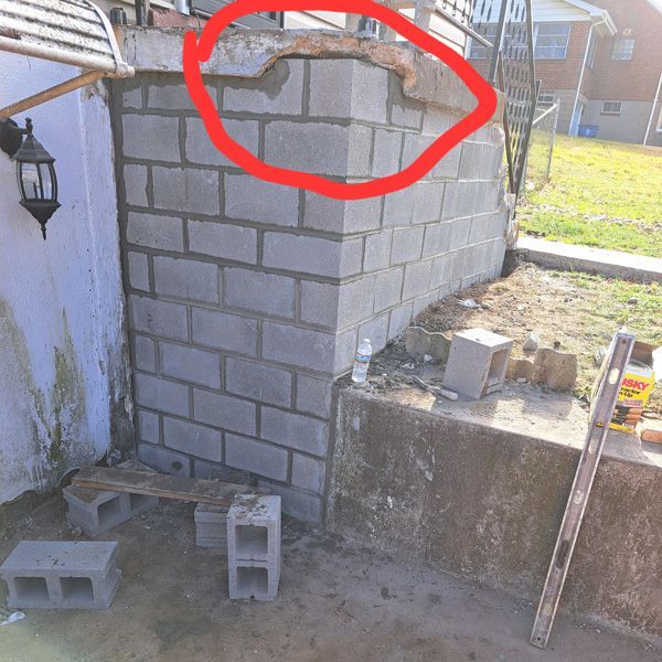 A cinder block wall in progress, the top is uneven and circled in red.  The wall is outdoors, adjacent to a patio and a grassy area.