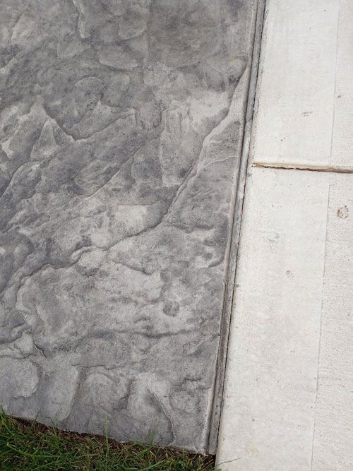 Close-up of textured gray concrete next to a light-colored, smooth surface. Green grass is visible at the bottom.