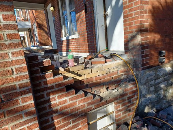 A partially demolished brick wall with exposed interior, possibly undergoing repair work. Bricks and debris litter the ground.