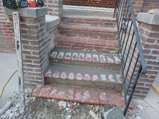 Brick steps being repaired. Mortar is being applied to the risers. A level and handrail are visible.
