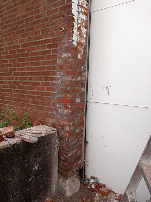 Brick wall meets white wall, with exposed brick and a concrete base visible.