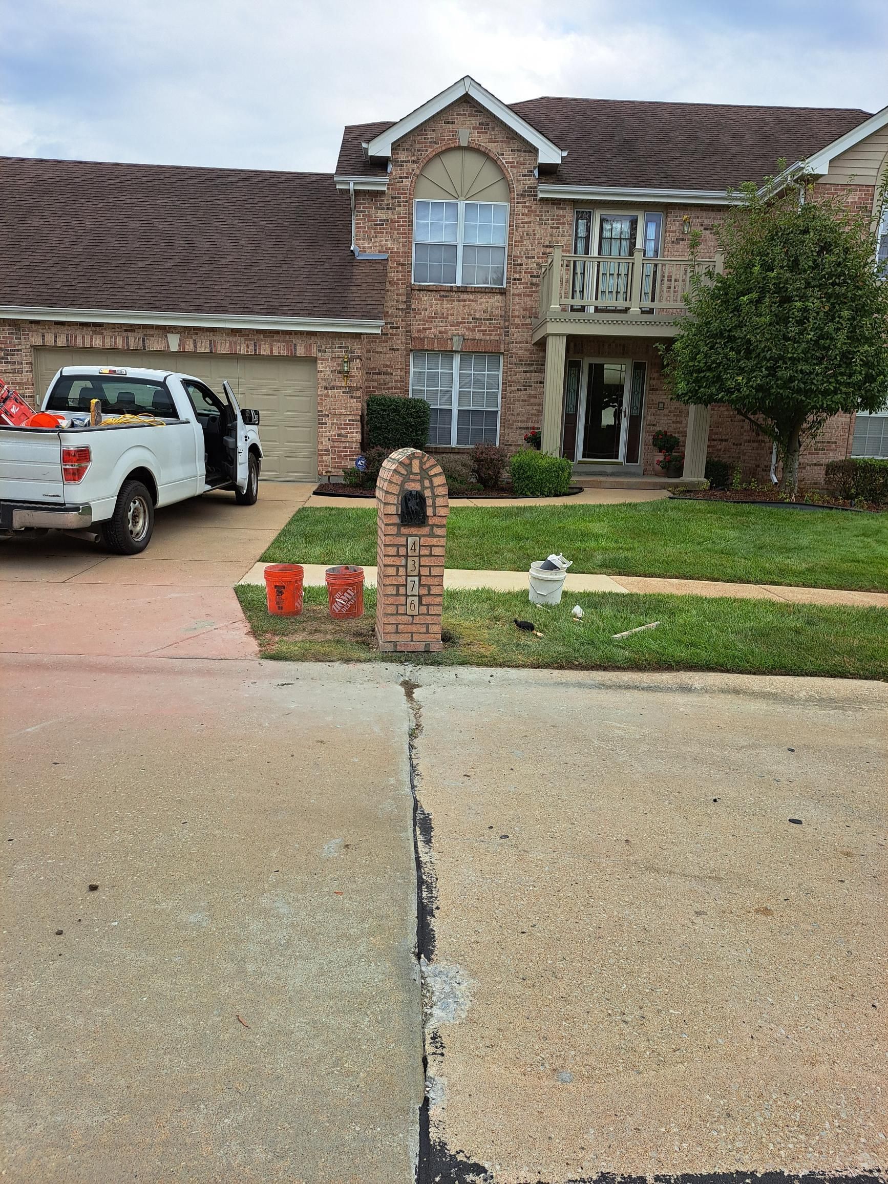 A two-story brick house with a cracked driveway; a white truck is parked in front.