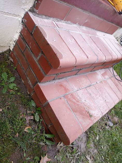 Brick steps leading up to a light-colored wall, set outdoors on grassy ground. The top step has a rounded edge.