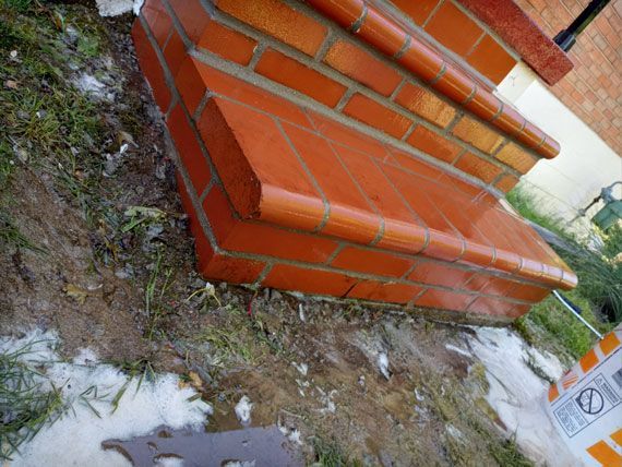 Brick steps with rounded edges, in a red-orange hue, are outdoors with wet ground and some patches of snow.