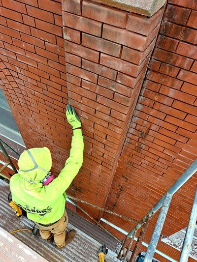 Person in neon green working on a red brick chimney, wearing a mask and gloves while standing on scaffolding.