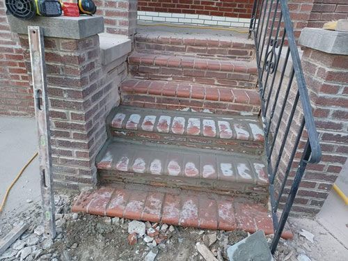 Brick steps being repaired, with gray concrete and tools present. The steps have a curved front.